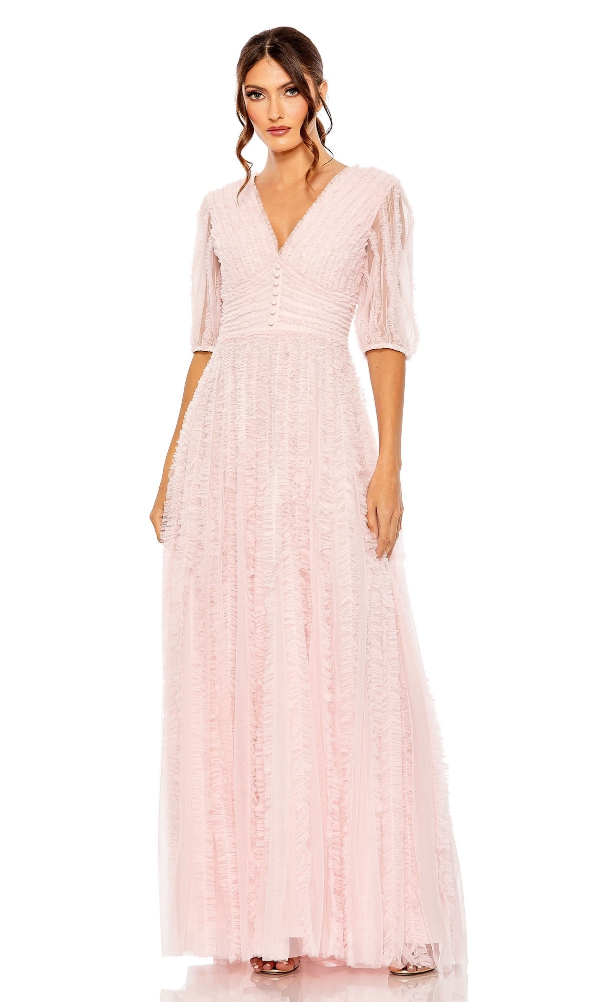 A woman stands against a white background wearing the Long Formal Dress 8050 by Mac Duggal, featuring a light pink textured A-line silhouette, elbow-length sleeves, V-neckline, and button details down the bodice.